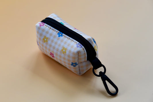 Small fabric pouch with floral pattern and black zipper on a beige background