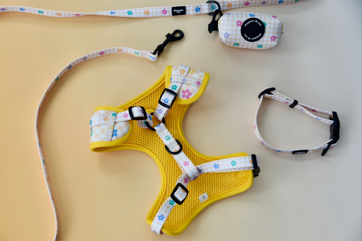 Yellow dog harness with floral patterned straps on a beige surface