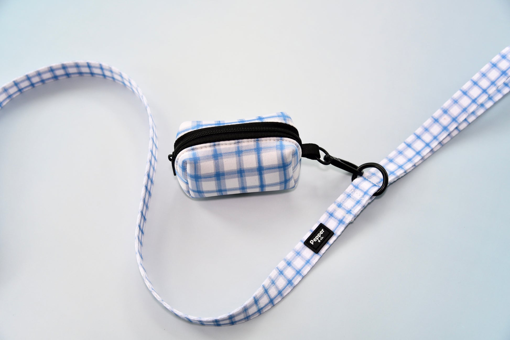 Blue and white checkered dog leash and pouch on a light background