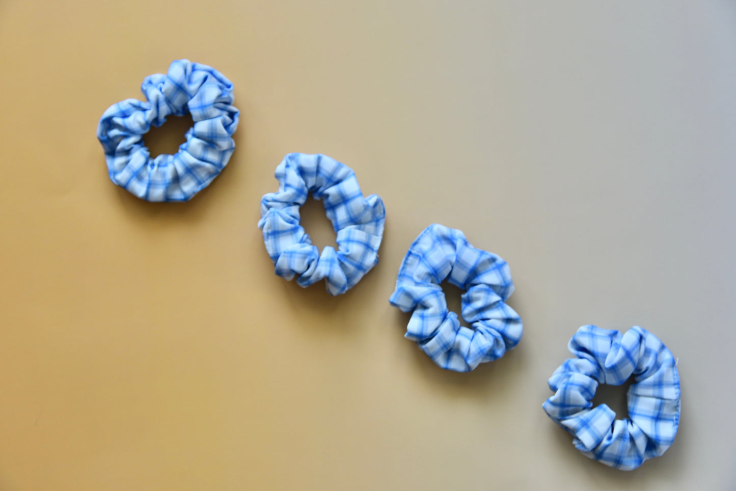 Four blue tie-dye scrunchies on a beige background