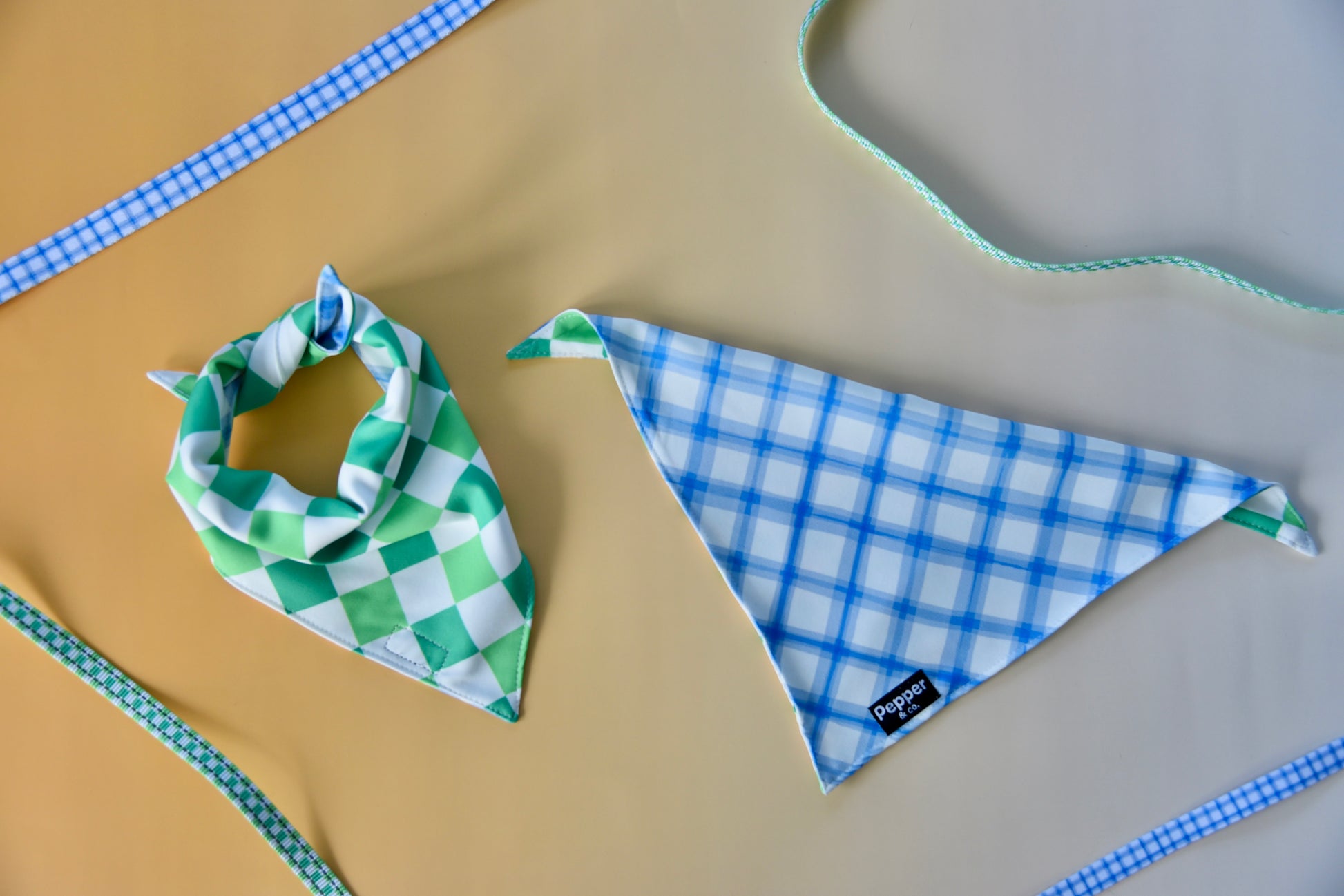 Two fabric bandanas, one green and white checkered, the other blue and white checkered, on a textured surface.