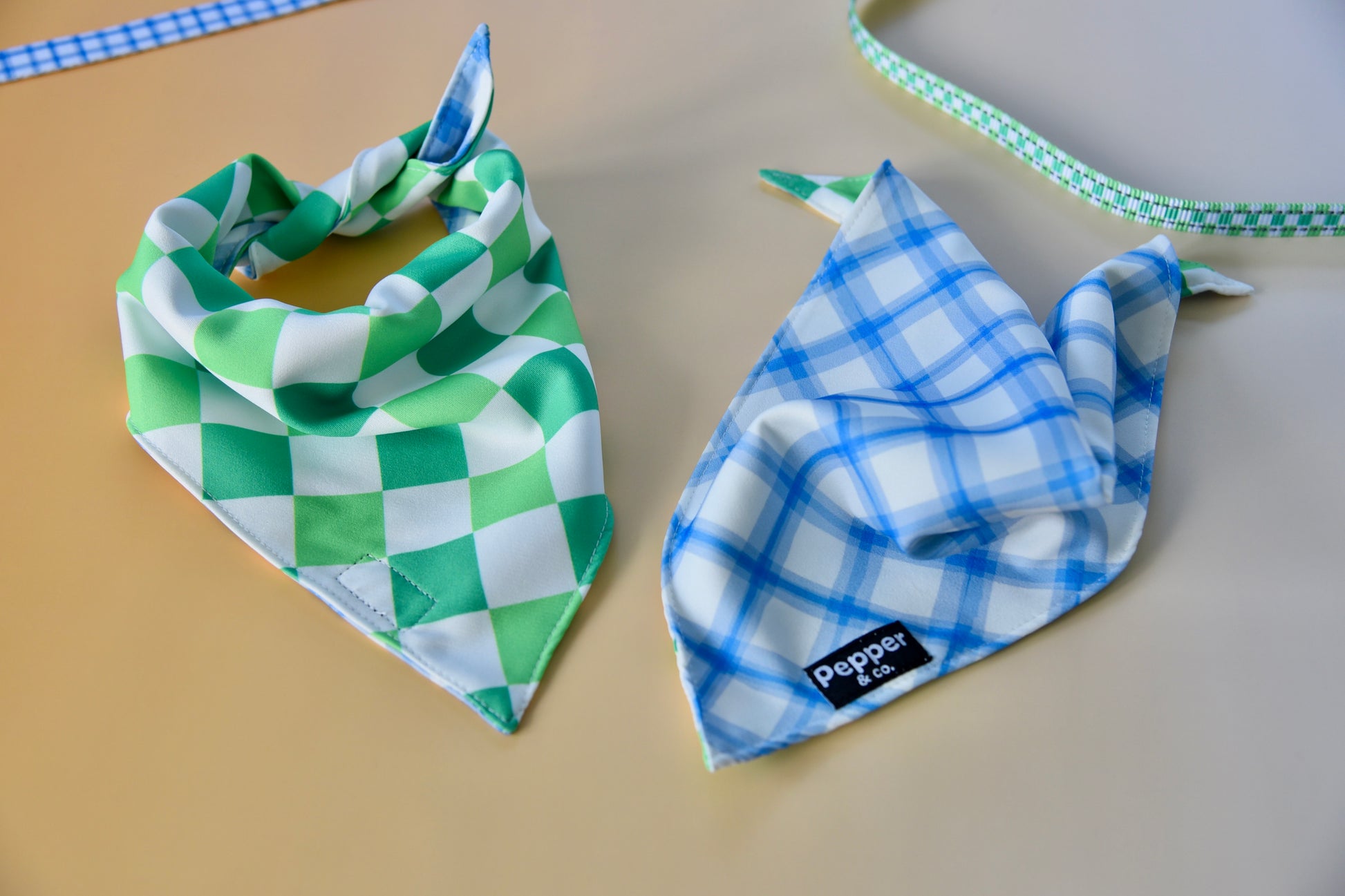 Two checkered bandanas, one green and white, the other blue and white, on a flat surface.