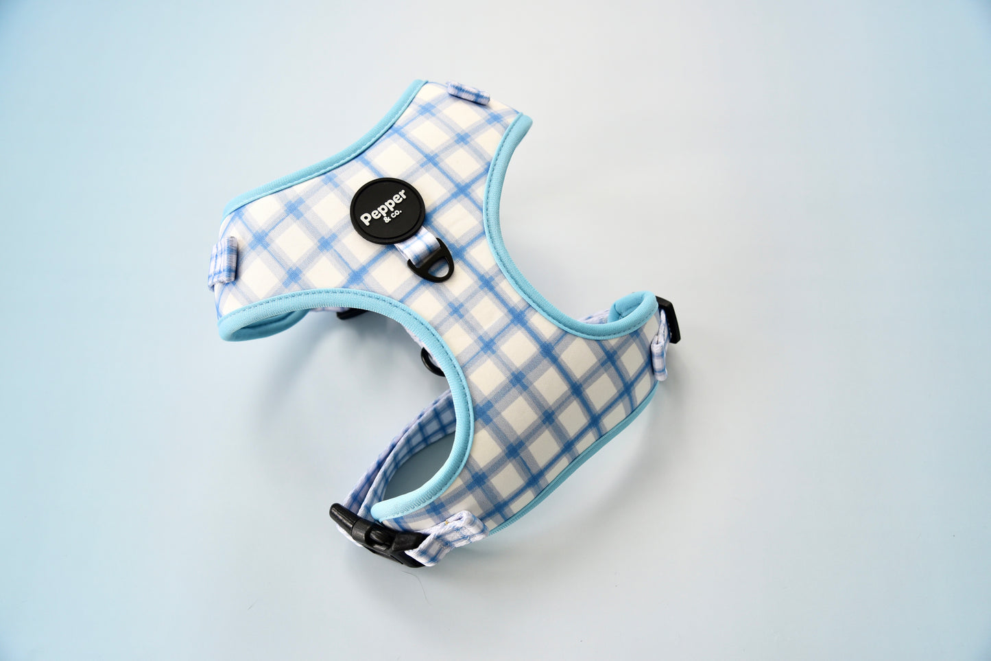 A blue and white checkered pet harness with a black buckle and trim, displayed against a neutral background