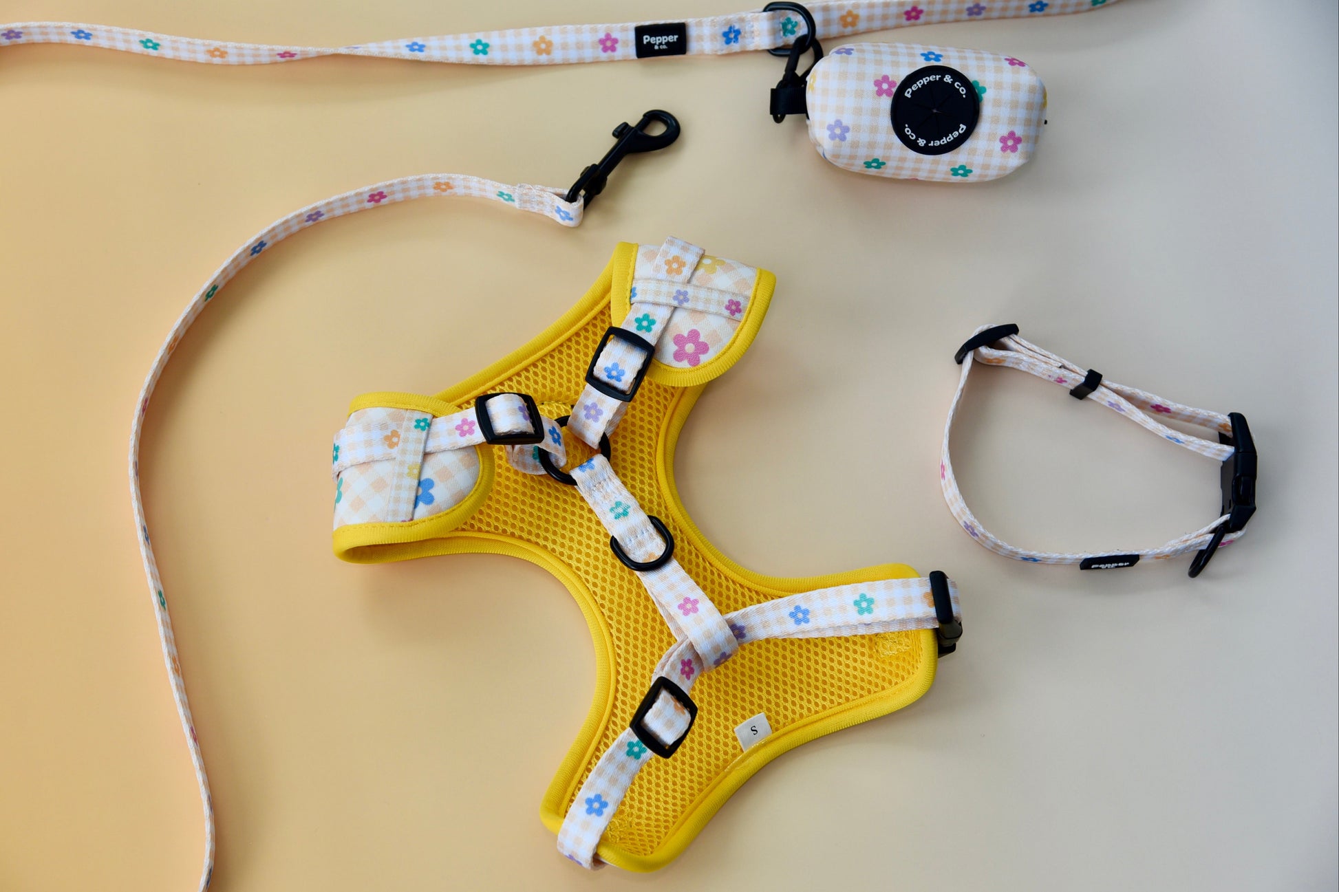 Yellow dog harness with floral patterned straps on a beige surface